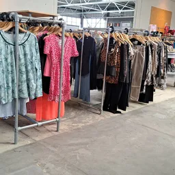 Rekken met tweedehands dameskleding in diverse kleuren en patronen in de winkel