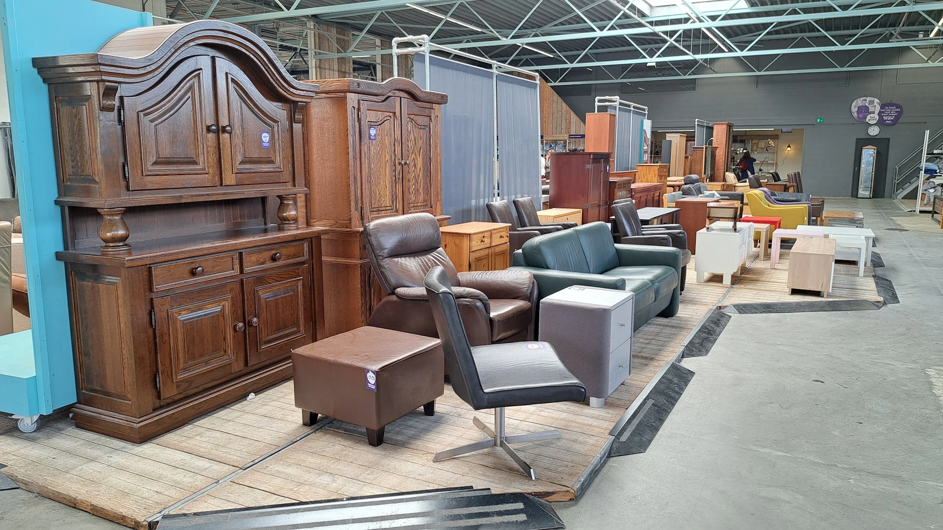 Uitgestalde meubels in een kringloopwinkel: houten kasten, fauteuils, poefs en zetels op de vloer