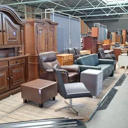 Uitgestalde meubels in een kringloopwinkel: houten kasten, fauteuils, poefs en zetels op de vloer
