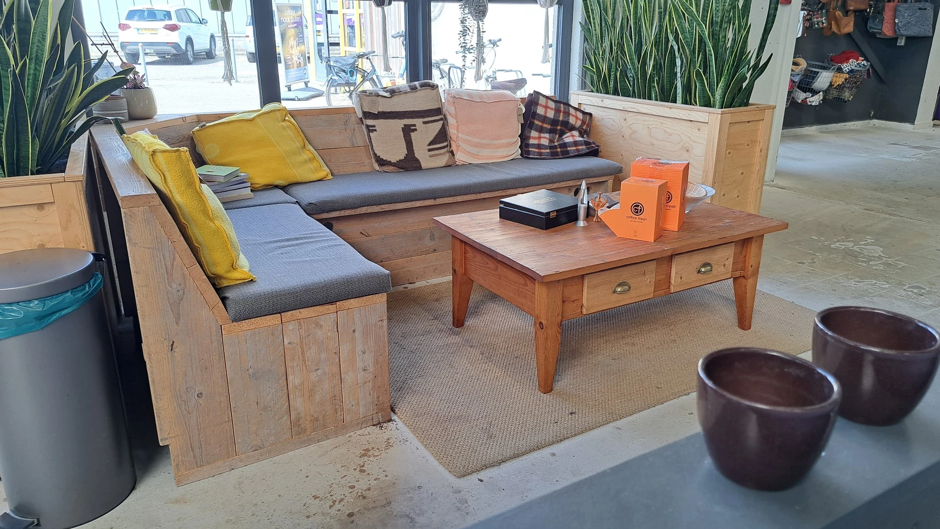 Houten zithoek met grijze en blauwe kussens, houten salontafel en decoratieve items in een kringloopwinkel