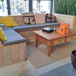 Houten zithoek met grijze en blauwe kussens, houten salontafel en decoratieve items in een kringloopwinkel