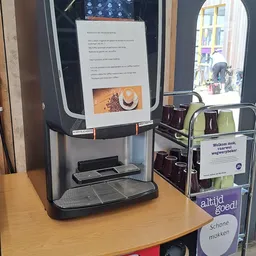 Zelfbedieningskoffieapparaat met donkere bonen en instructiepaneel op houten tafel