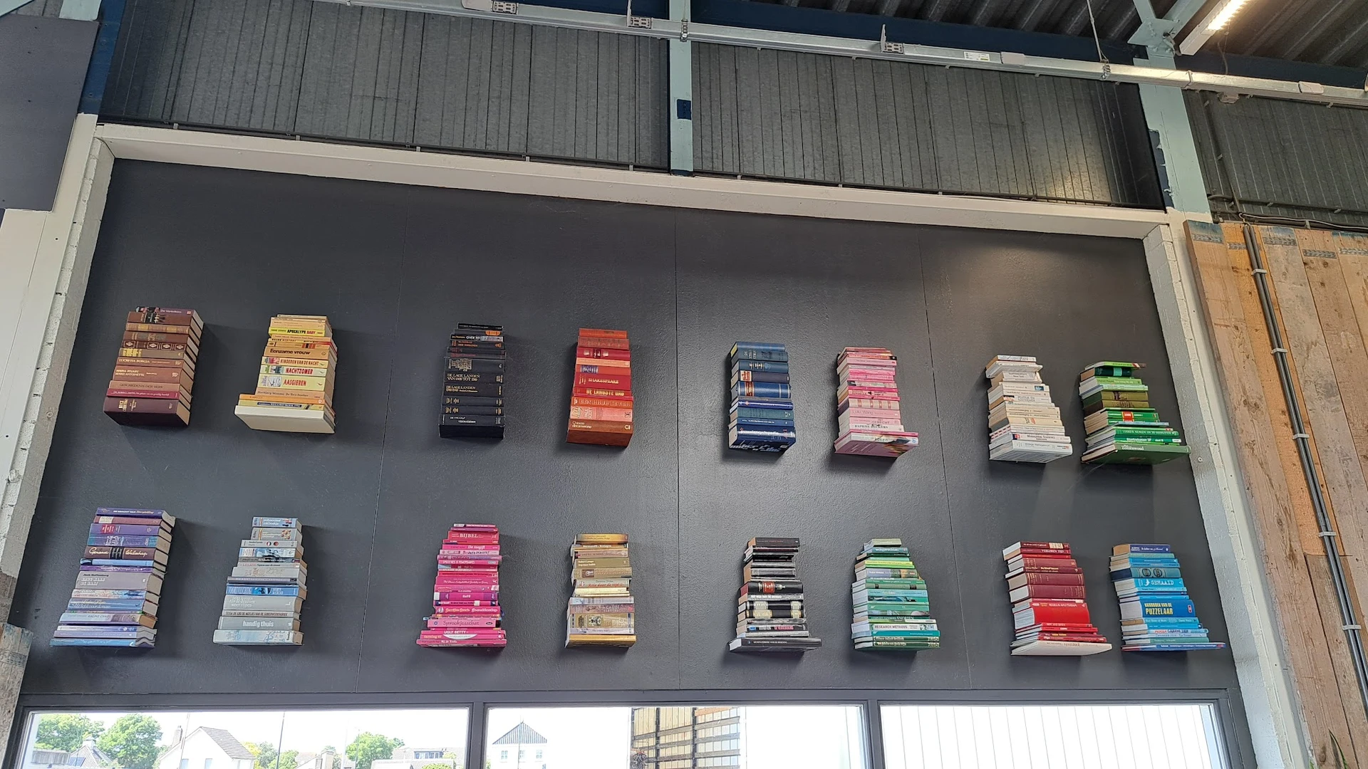 Muurdisplay met gestapelde boeken in verschillende kleuren en formaten op grijze wand.