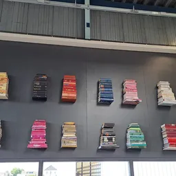 Muurdisplay met gestapelde boeken in verschillende kleuren en formaten op grijze wand.