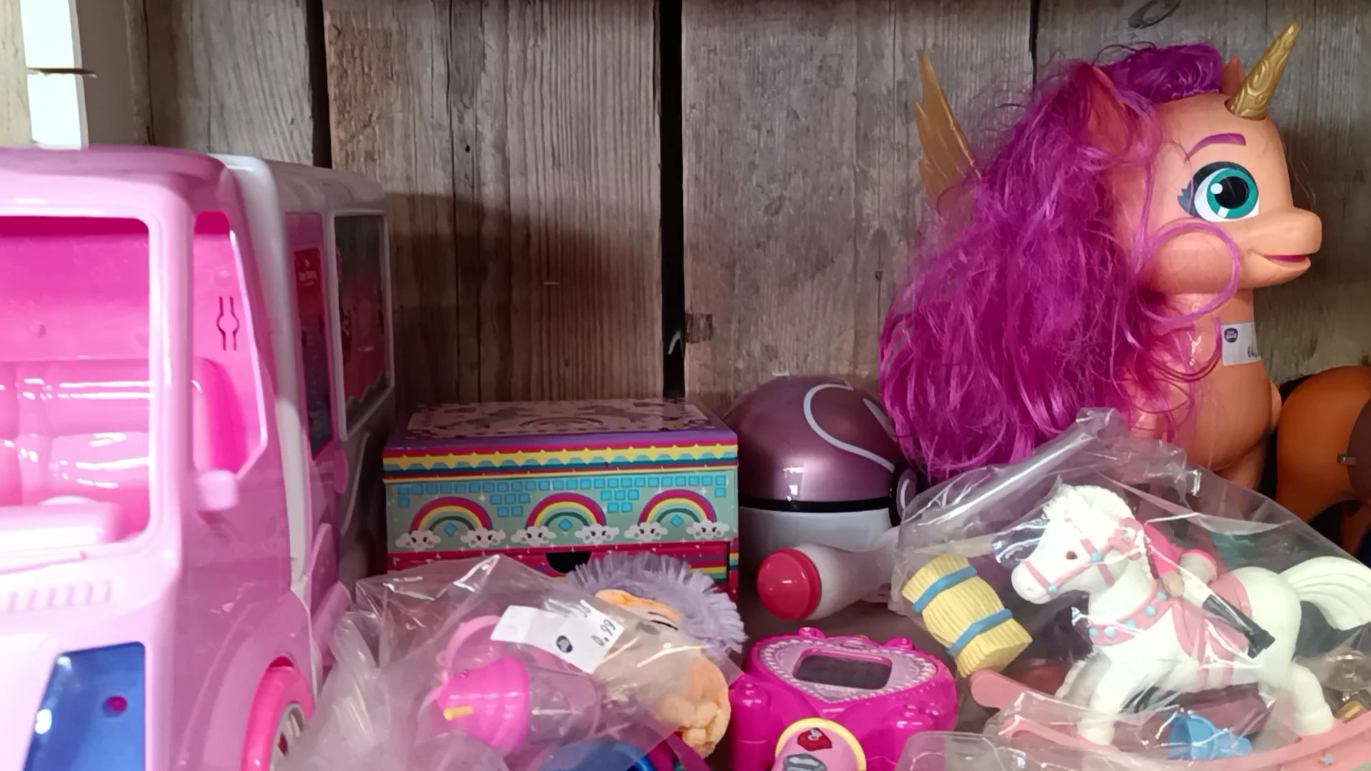 Kinderspeelgoed en poppen uitgestald op een plank, inclusief roze speelgoedkeuken en paarse pruik