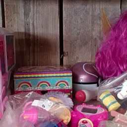 Kinderspeelgoed en poppen uitgestald op een plank, inclusief roze speelgoedkeuken en paarse pruik