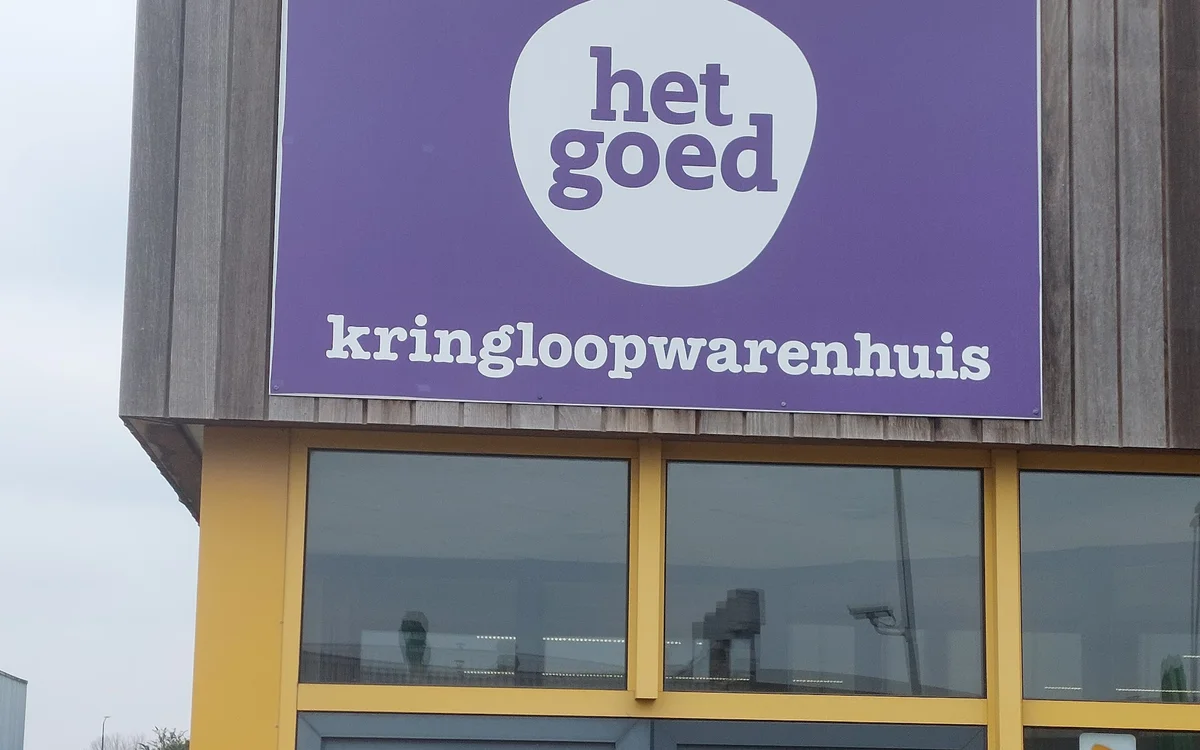 Gevel van kringloopwinkel met paars bord met 'het goed' logo en 'kringloopwarenhuis' tekst, gele raamkozijnen