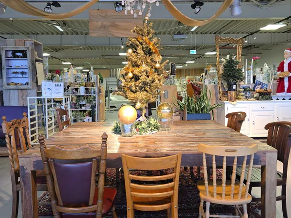 Winkelinterieur met houten eettafel, stoelen, gouden kerstboom en diverse meubels en decoratie