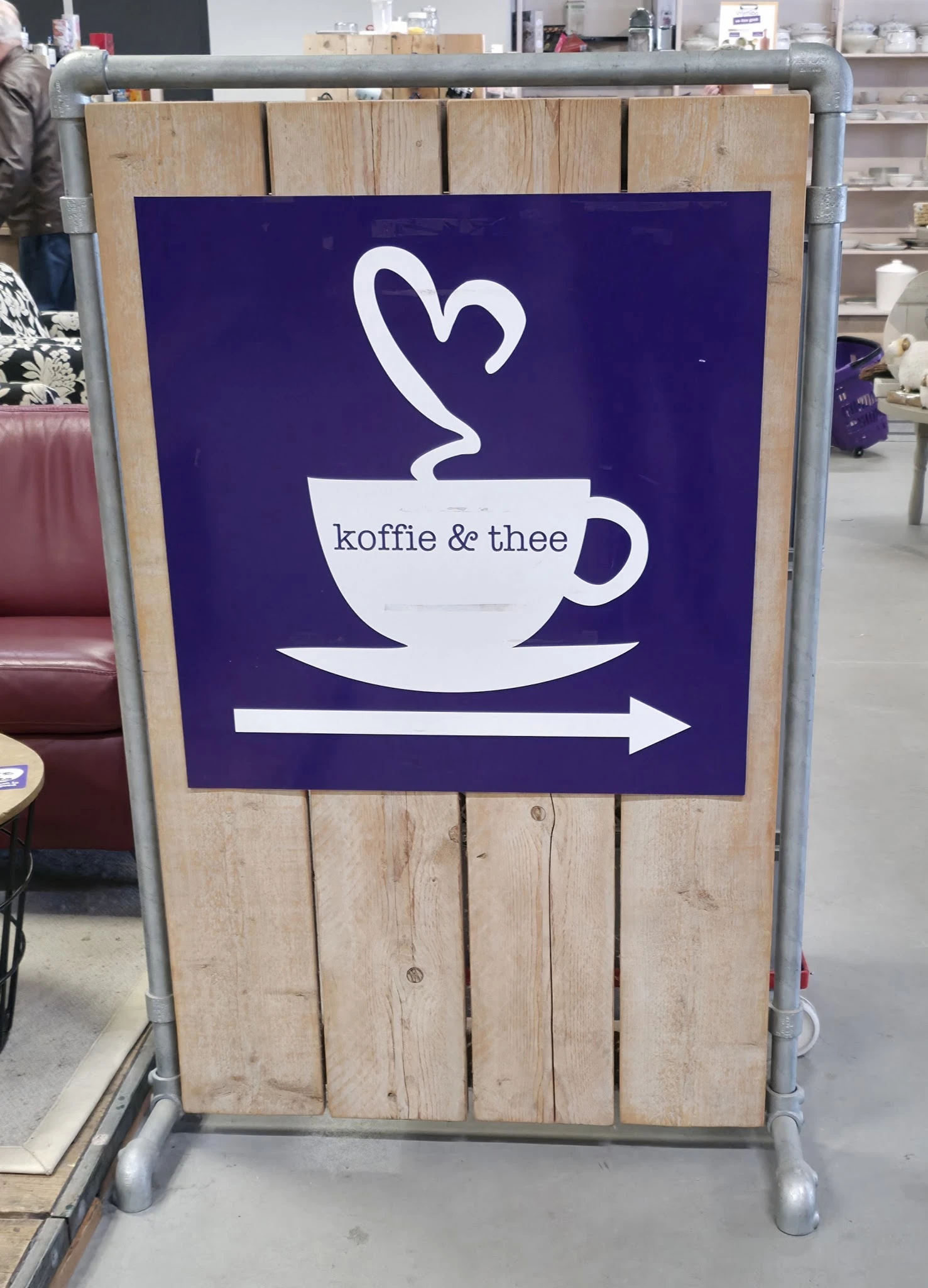 Bord met logo en tekst 'koffie & thee' met pijl, aanduiding van de lunchroom in de winkel