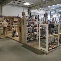 Overzicht van kringloopwinkel met houten en witte stellingen vol huishoudartikelen, decoratie en diverse goederen