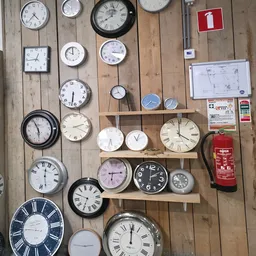 Verzameling van diverse wandklokken en klokken op houten wanden en planken, met verschillende stijlen en maten
