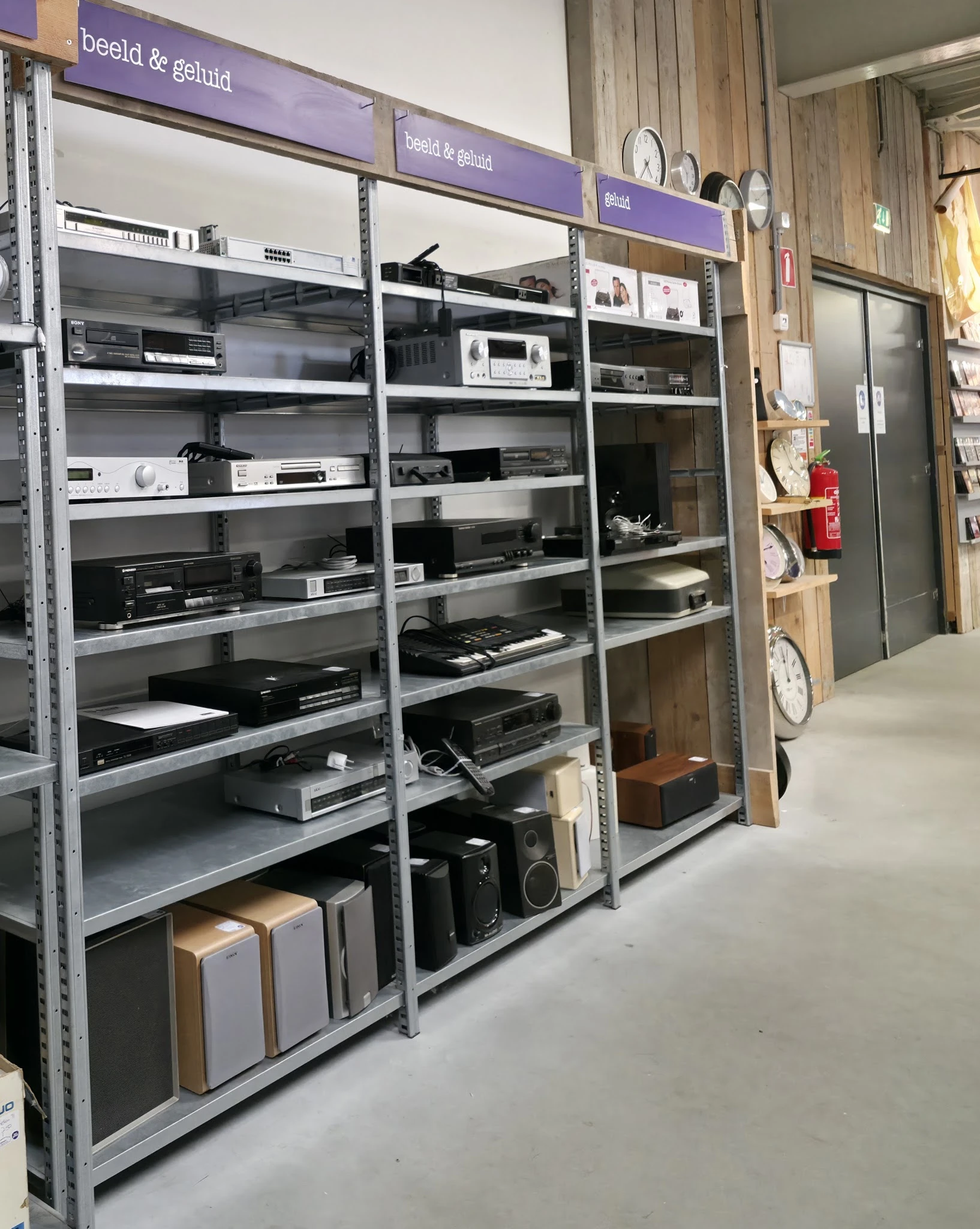 Metalen stellingen met diverse elektronische apparaten en audio-apparatuur in kringloopwinkel