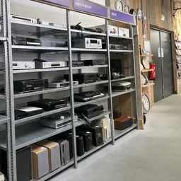 Metalen stellingen met diverse elektronische apparaten en audio-apparatuur in kringloopwinkel