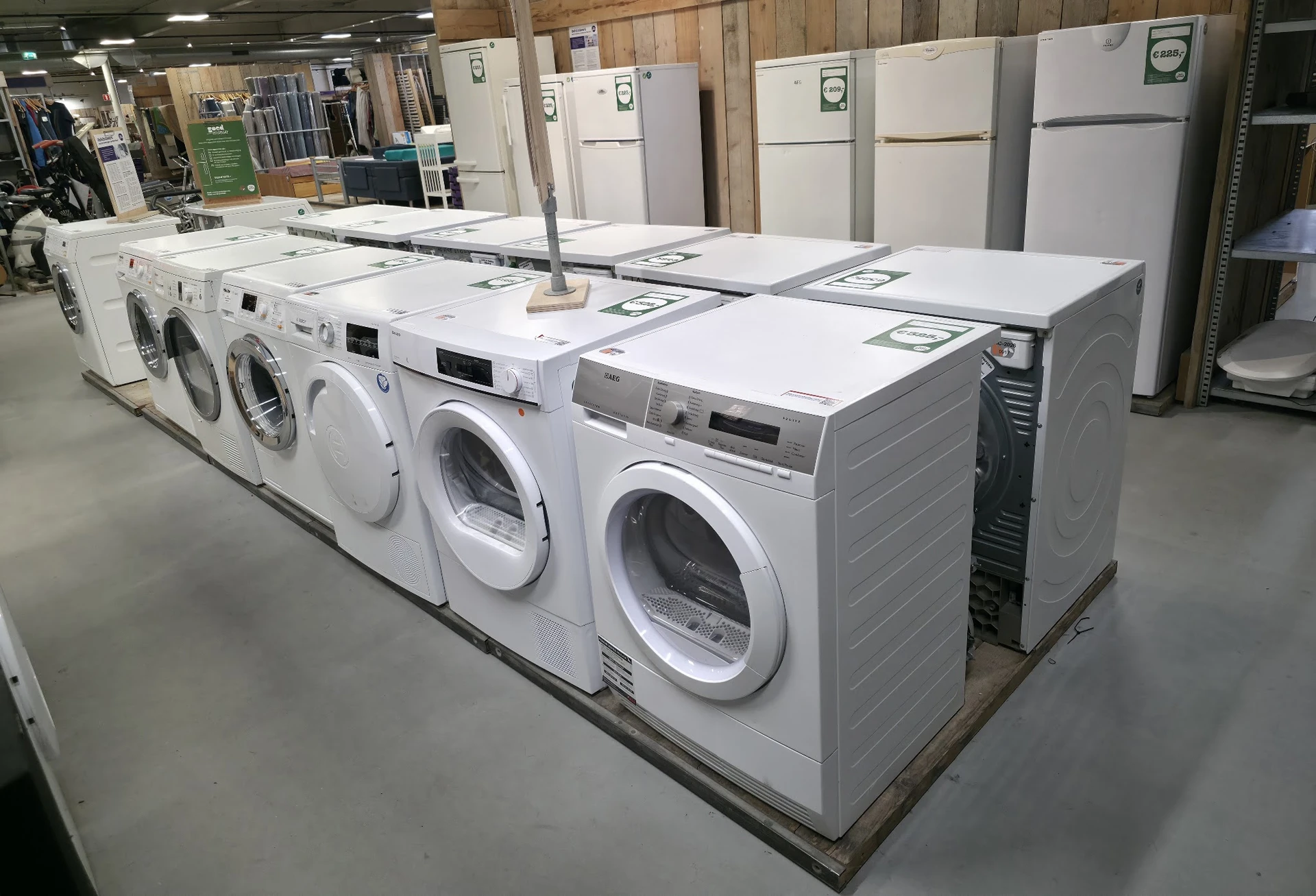 Rij met witte wasmachines en droogkasten uitgestald in een kringloopwinkel
