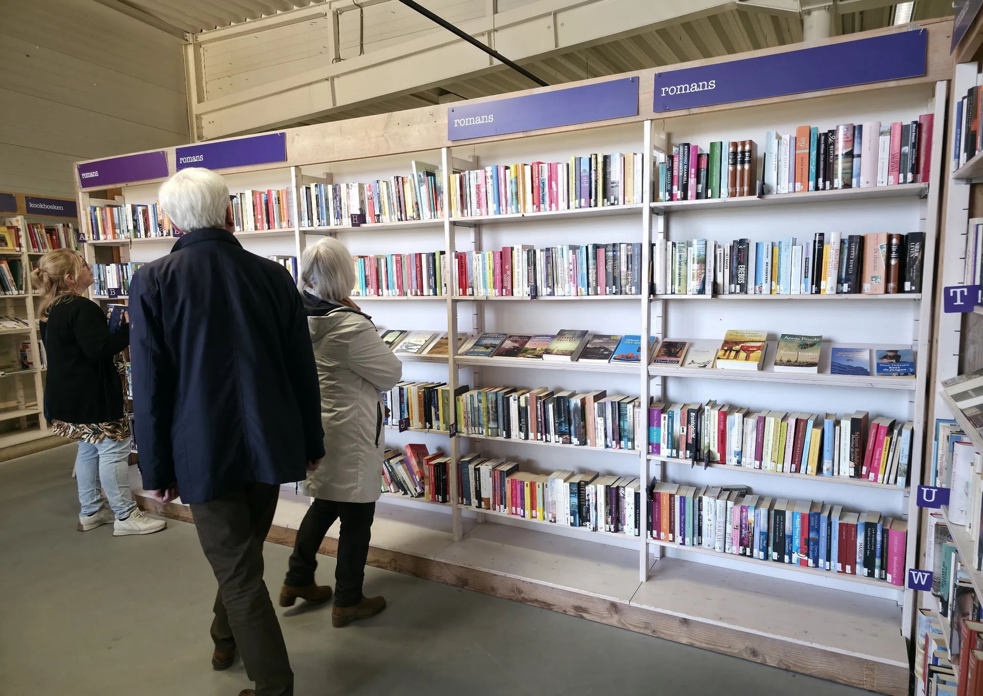 Bezoekers bekijken boekenrekken met boeken in een kringloopwinkel