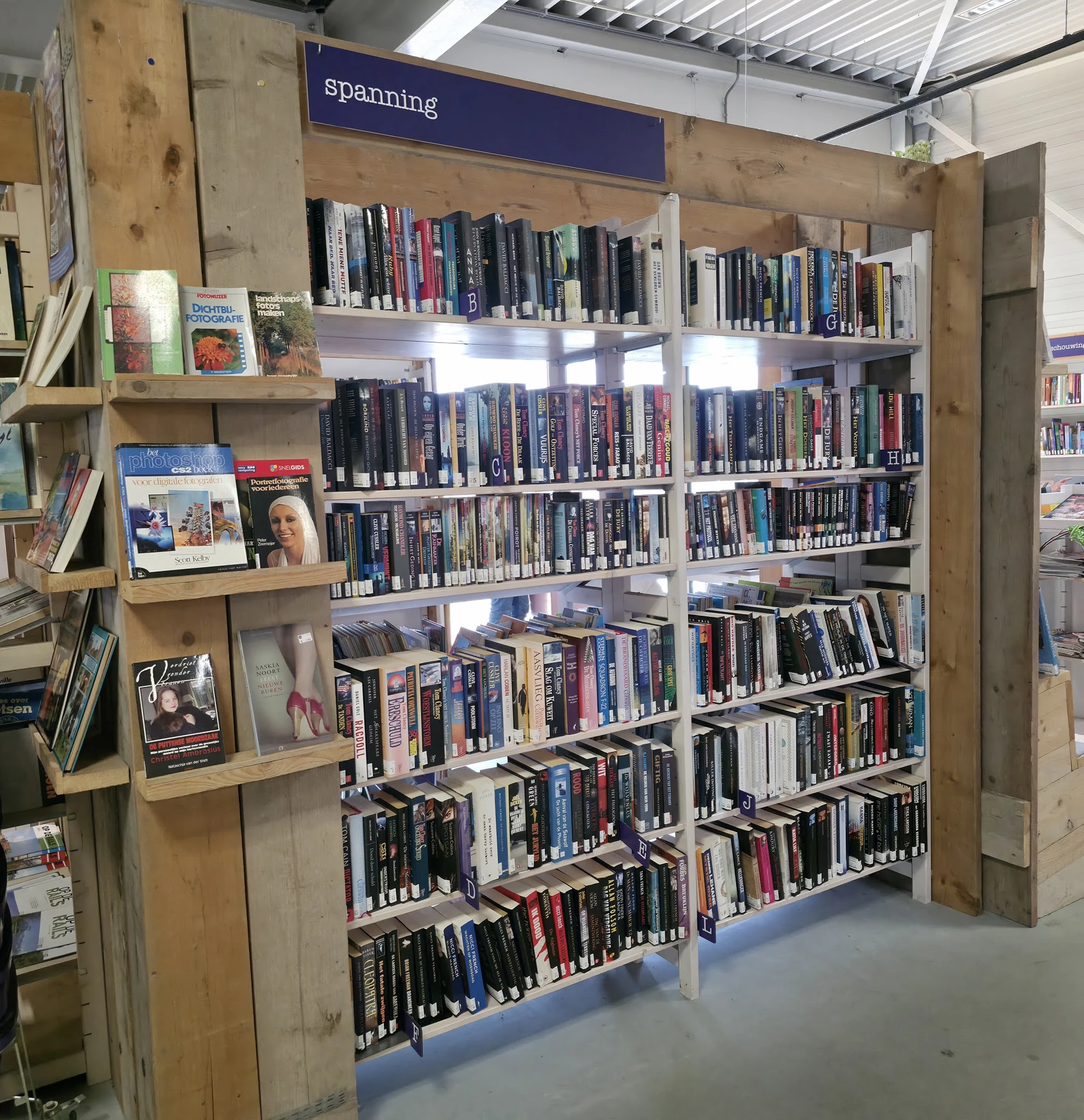Stellingen vol met dvd's en blu-rays in een kringloopwinkel, naast een klein display met boeken