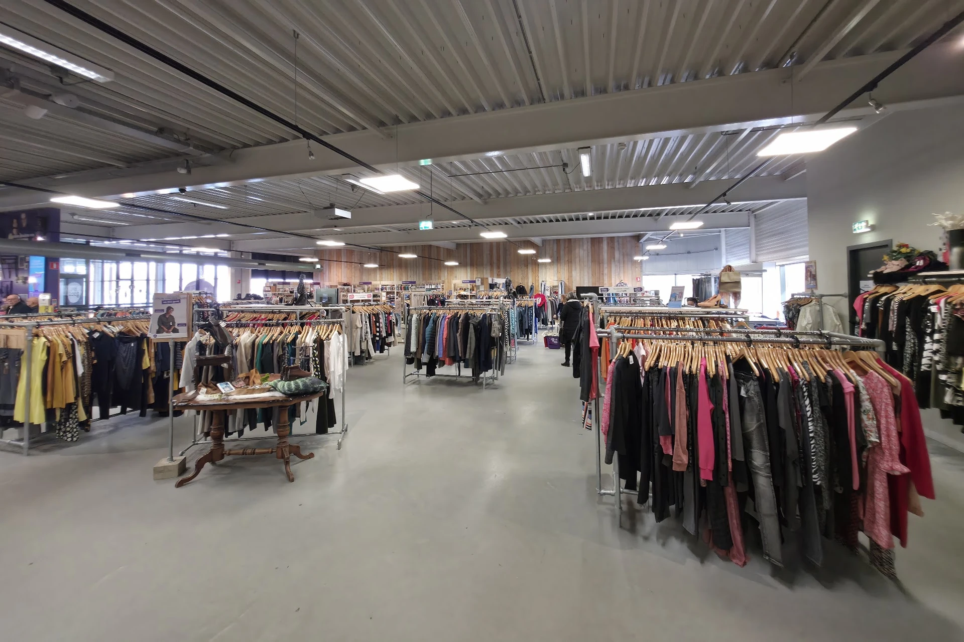 Winkelvloer met rekken vol tweedehands kleding, goed verlicht met moderne plafondverlichting