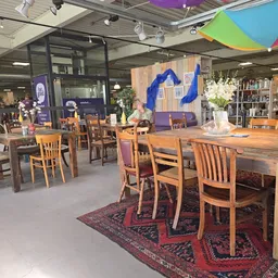 Interieur van kringloopwinkel met houten tafels, stoelen, blauwe wanddecoratie en plantenbakken
