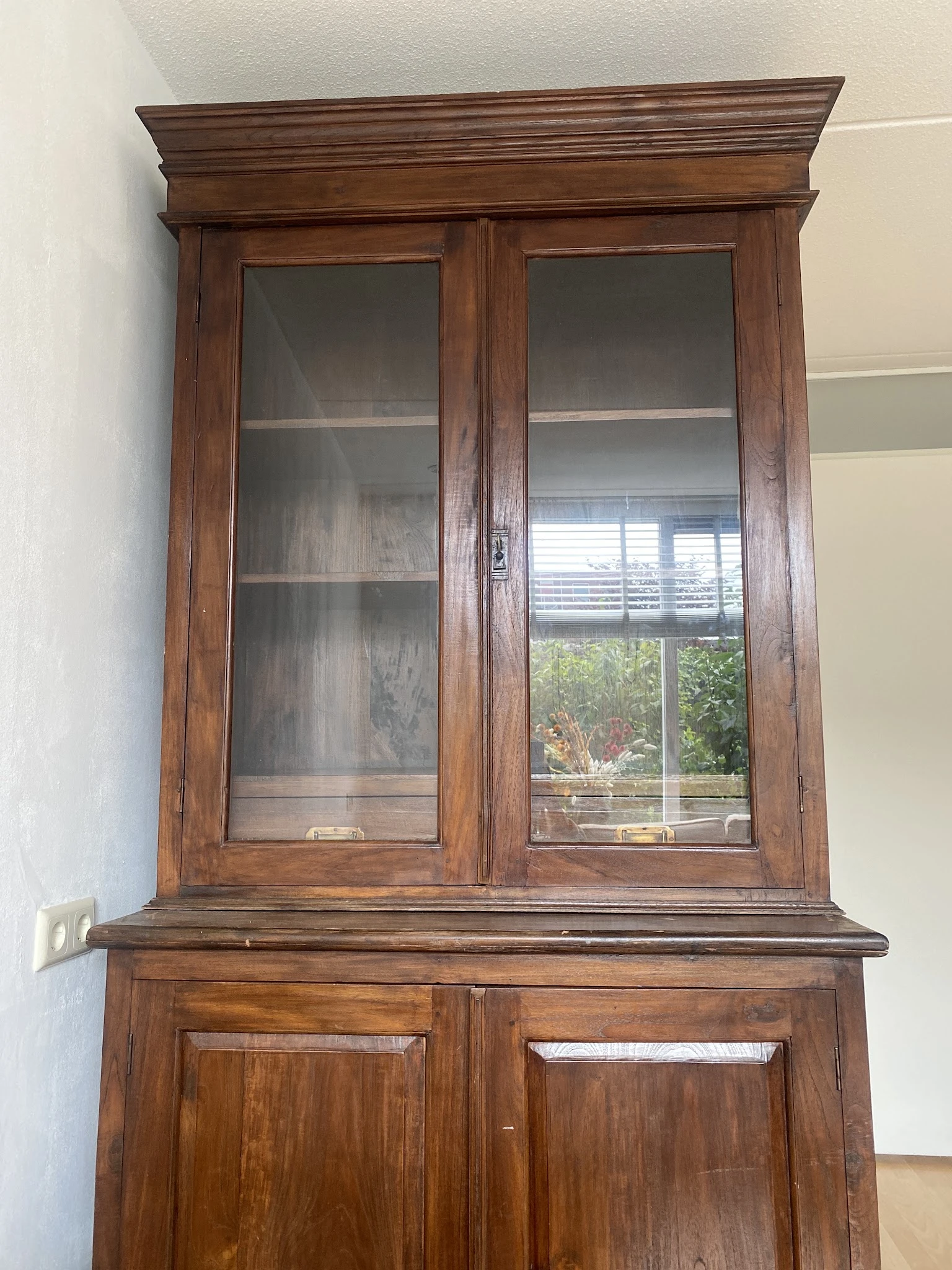 Houten glazen vitrinekast met twee deuren en drie legplanken, tegen witte wand gemonteerd
