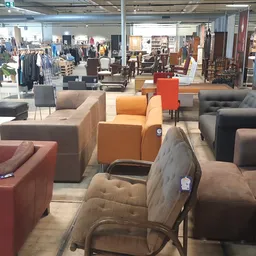 Winkelvloer met diverse meubels: rode, oranje en grijze zitmeubels, stoelen en banken, op de achtergrond kleding en meer wink