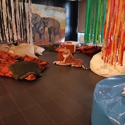 Speelgoedafdeling met knuffels, kleurrijke linten, een olifantenschilderij en speelmatten op donkere vloer