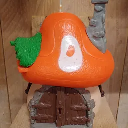 Close-up van een oranje speelgoedfiguur met groen blad en wit detail op de borst