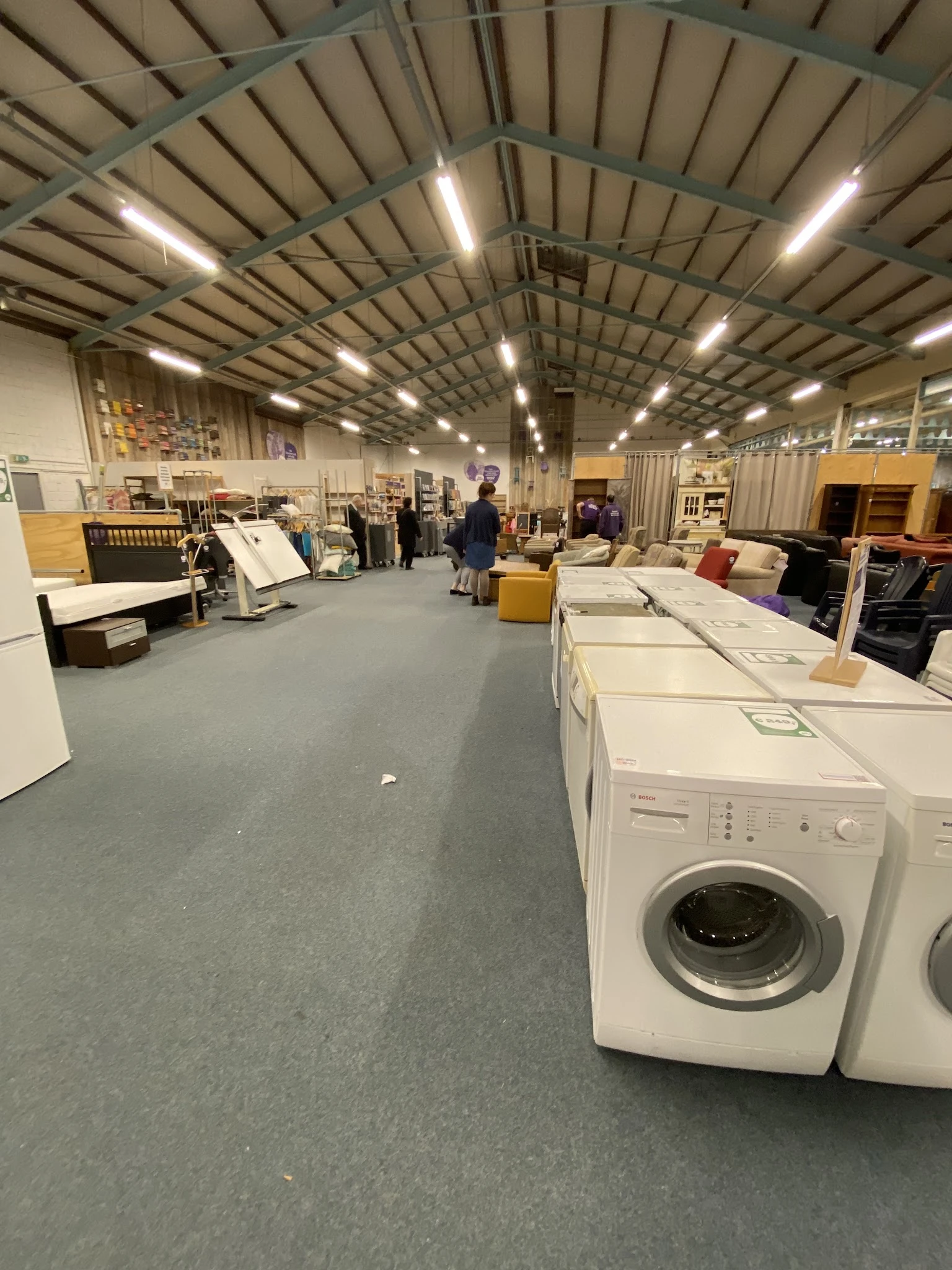 Winkelvloer met witgoed zoals wasmachines, kasten en meubels in een groot magazijn met industrieel plafond