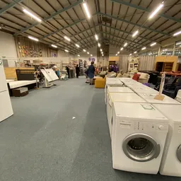 Winkelvloer met witgoed zoals wasmachines, kasten en meubels in een groot magazijn met industrieel plafond