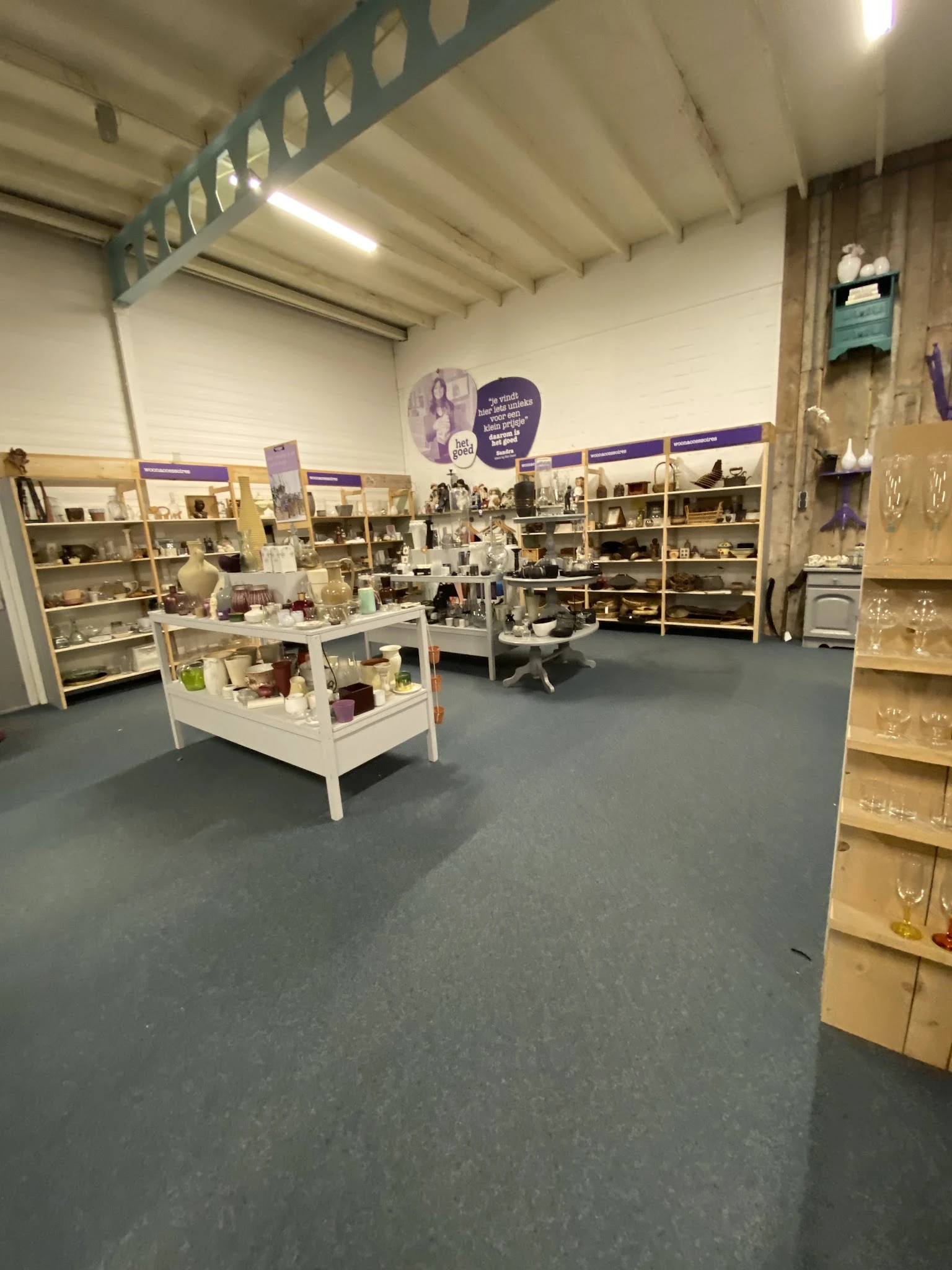 Winkelinterieur met houten stellingen vol decoratieve items en serviesgoed, witte displaykasten op de vloer en paarse decorat