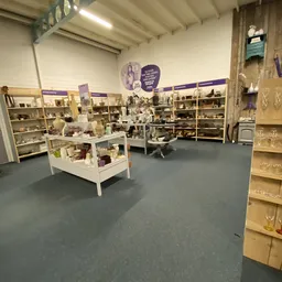 Winkelinterieur met houten stellingen vol decoratieve items en serviesgoed, witte displaykasten op de vloer en paarse decorat