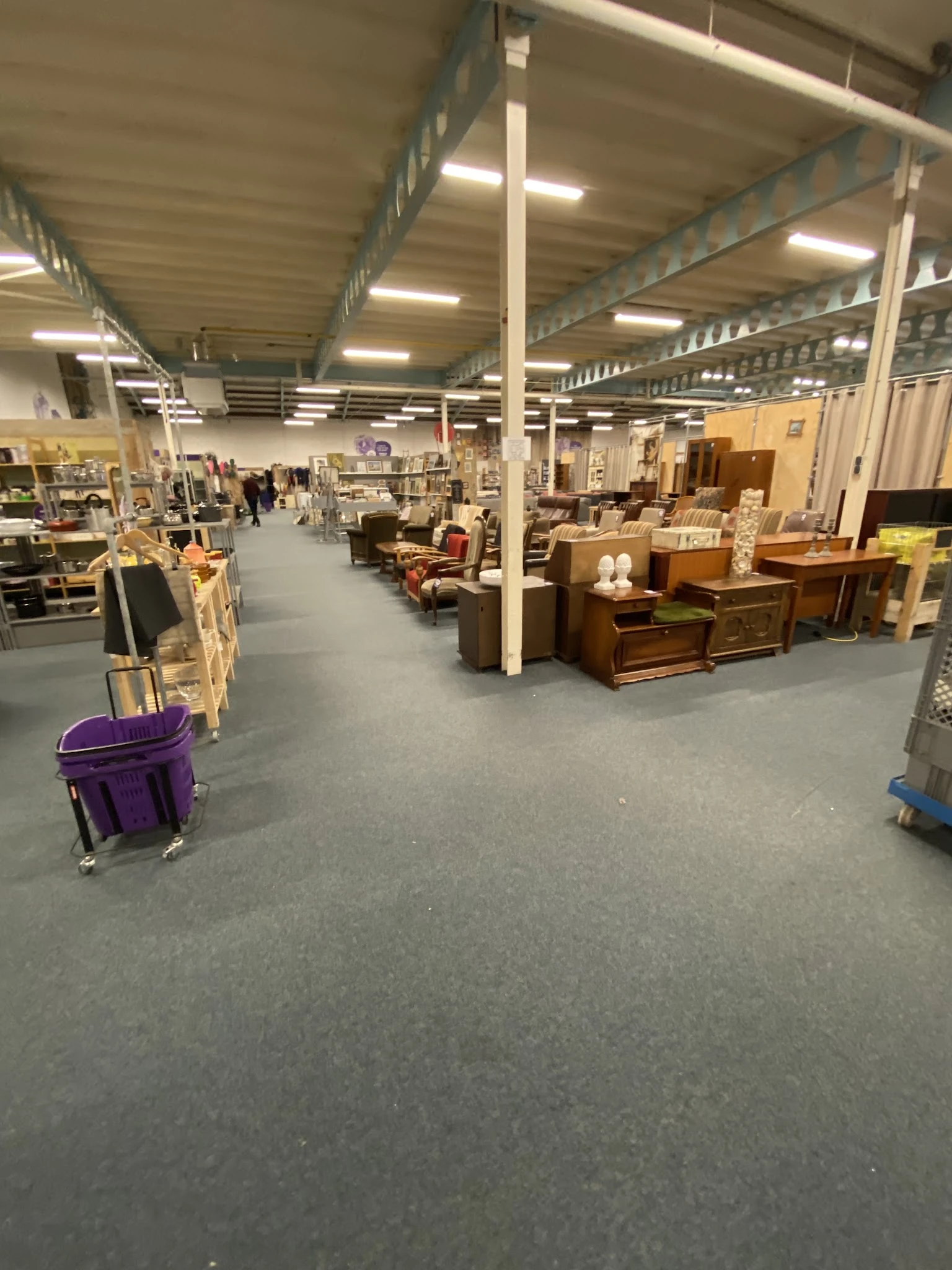 Spacious warehouse interior with wooden furniture, storage boxes, and various secondhand items displayed throughout the sales
