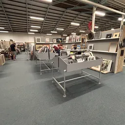 Winkelvloer met grijze tafelstellages, stellingkasten en expositiewanden met ingelijste kunstwerken en decoratieve items