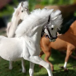 Witte pluchen speelgoedpaard met zwart tuigje en bruine speelgoedpaarden op achtergrond