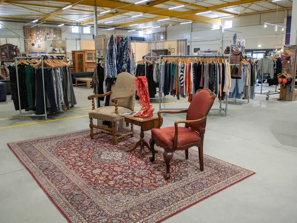 Winkelvloer met kledingrekken, vintage meubels en een Perzisch tapijt met twee stoelen in de voorgrond