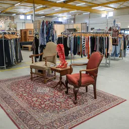 Winkelvloer met kledingrekken, vintage meubels en een Perzisch tapijt met twee stoelen in de voorgrond