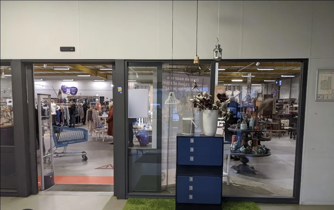 Winkelinterieur met glazen deuringang, blauwe kastjes en uitzicht op kledingrekken en winkelvloer