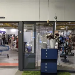 Winkelinterieur met glazen deuringang, blauwe kastjes en uitzicht op kledingrekken en winkelvloer