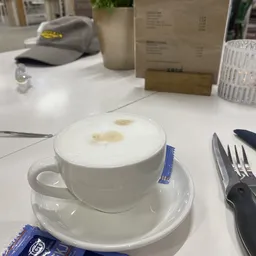 Kopje cappuccino met melkschuim op een witte schotel, met bestek en tafelgerei