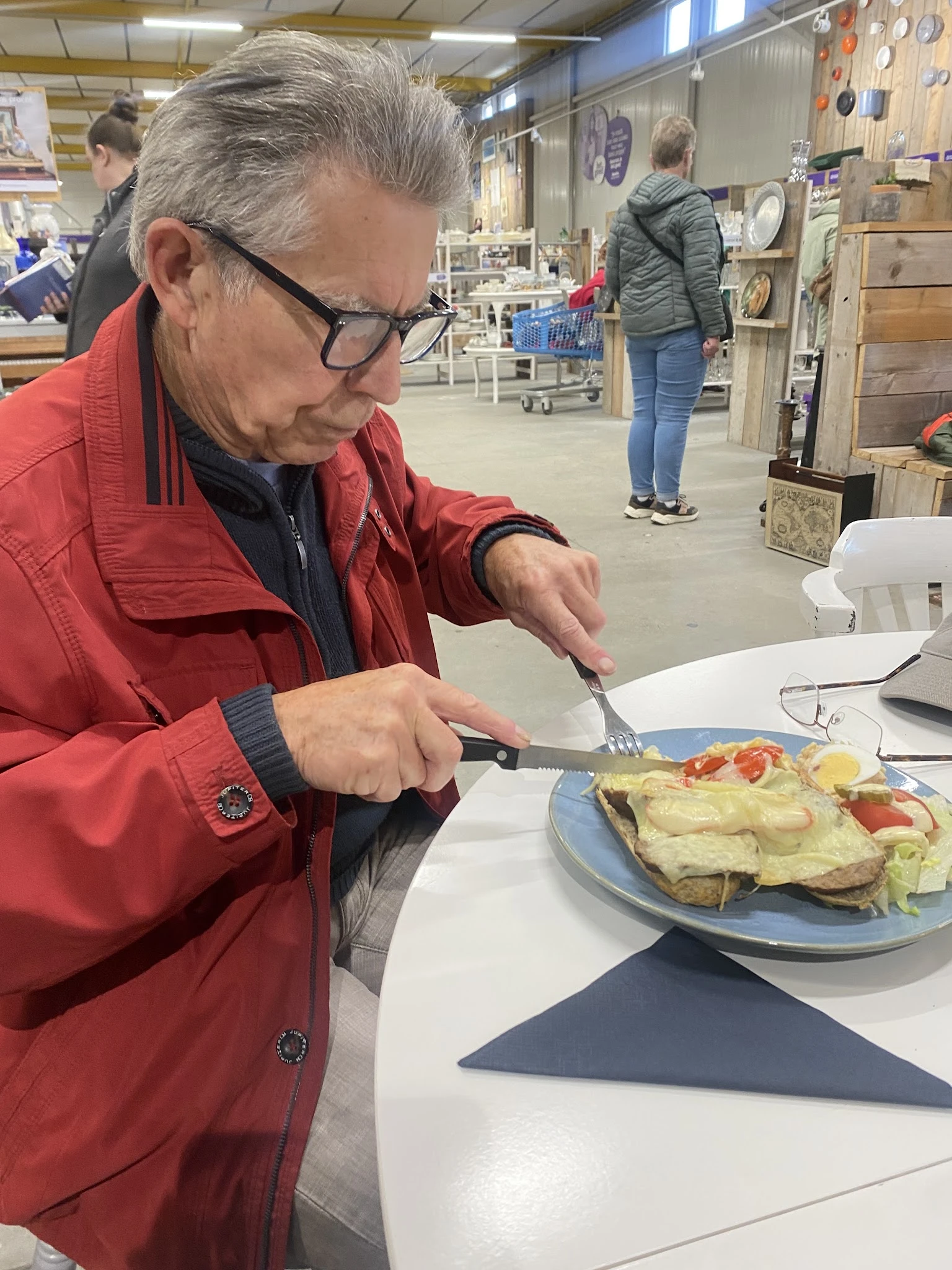 Man in rood jasje eet een omelet met groenten uit een blauwe schaal in de lunchroom