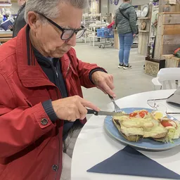 Man in rood jasje eet een omelet met groenten uit een blauwe schaal in de lunchroom