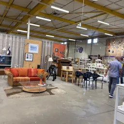 Winkelvloer met oranje bank, stoelen, diverse meubels en spullen uitgestald in een groot magazijnachtig ruimte met industriee