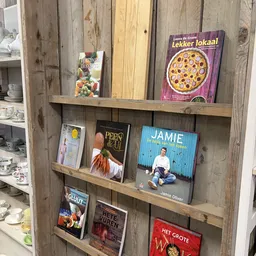 Houten stellage met uitgestal kookboeken en culinaire boeken, waaronder titels van Jamie Oliver en 'Lekker lokaal'
