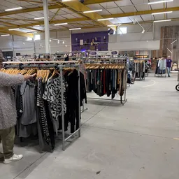 Rekken met tweedehands kleding op houten hangers in een ruime winkelhal