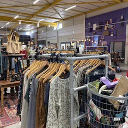 Rekken met tweedehands kleding op houten hangertjes in een kringloopwinkel