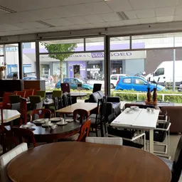Eethoek met ronde en rechthoekige tafels en stoelen in een kringloopwinkel, uitzicht op straat door grote ramen