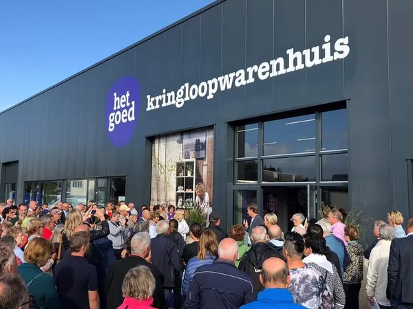 Gevel van kringloopwinkel met neonlogo en grote groep bezoekers bij de ingang