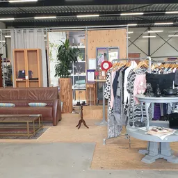 Winkelinterieur met bruine vintage bank, kledinrekken, witte display-tafel en houten meubels
