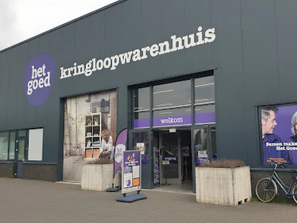 Grijze gevel van kringloopwinkel met paarse accenten, grote ramen en ingang met welkomstbord