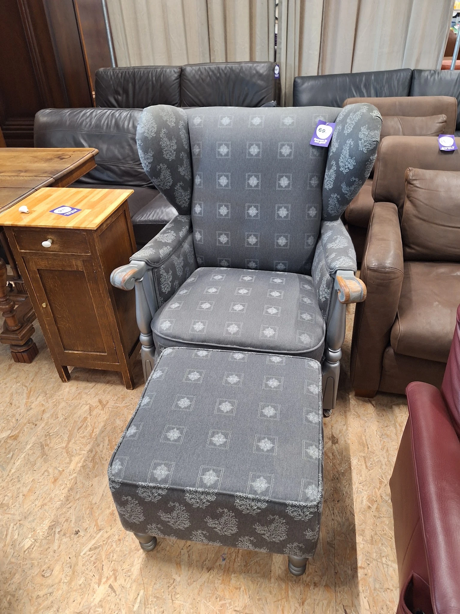 Grijze fauteuil met voetenbankje en houten armleuningen in een kringloopwinkel