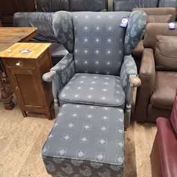 Grijze fauteuil met voetenbankje en houten armleuningen in een kringloopwinkel